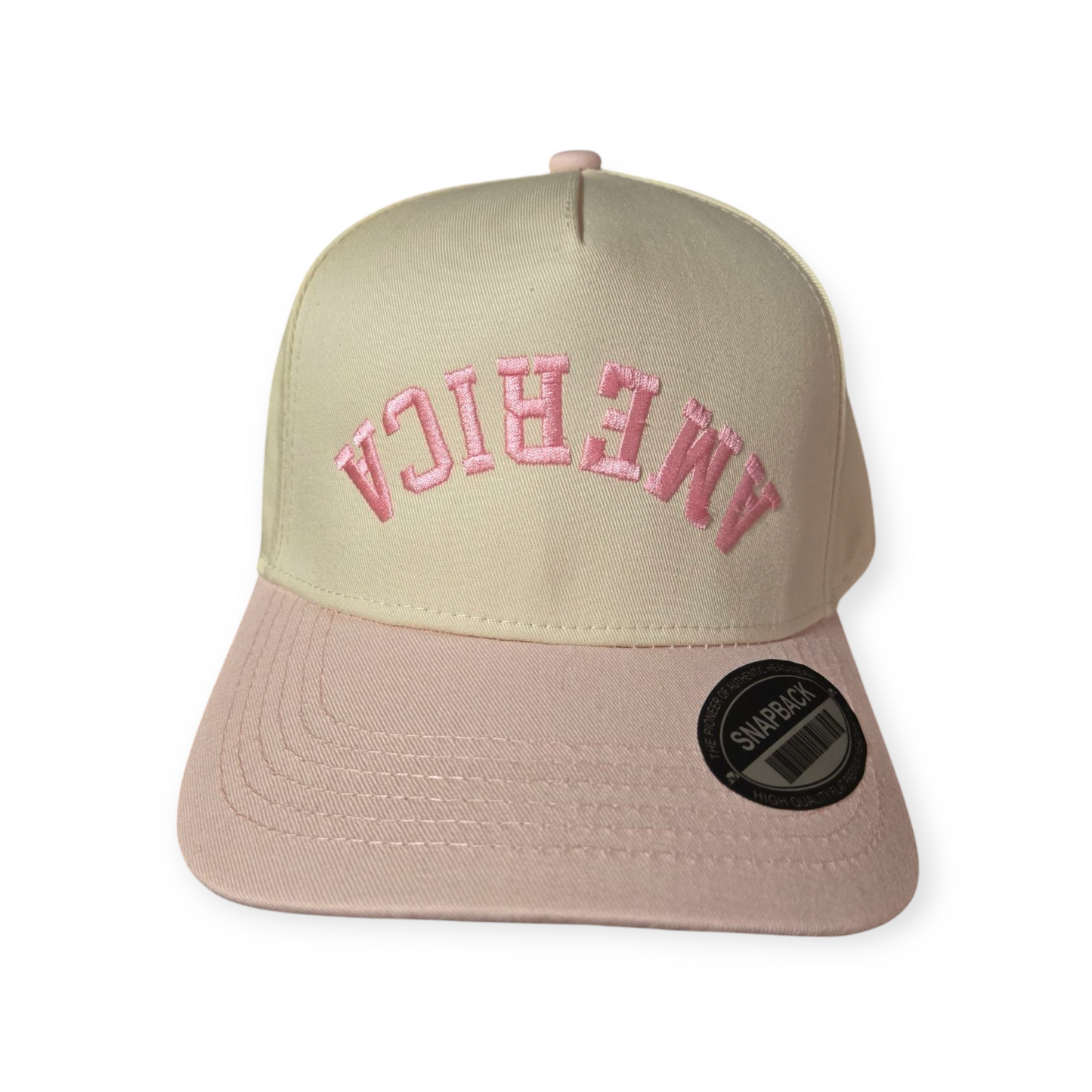 Front facing America Upside Down V1 structured hat in pink and beige with the word “America” embroidered upside down in pink on the front.