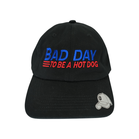 Front facing view of a black dad hat with “Bad Day to Be a Hot Dog” embroidered in blue and red.