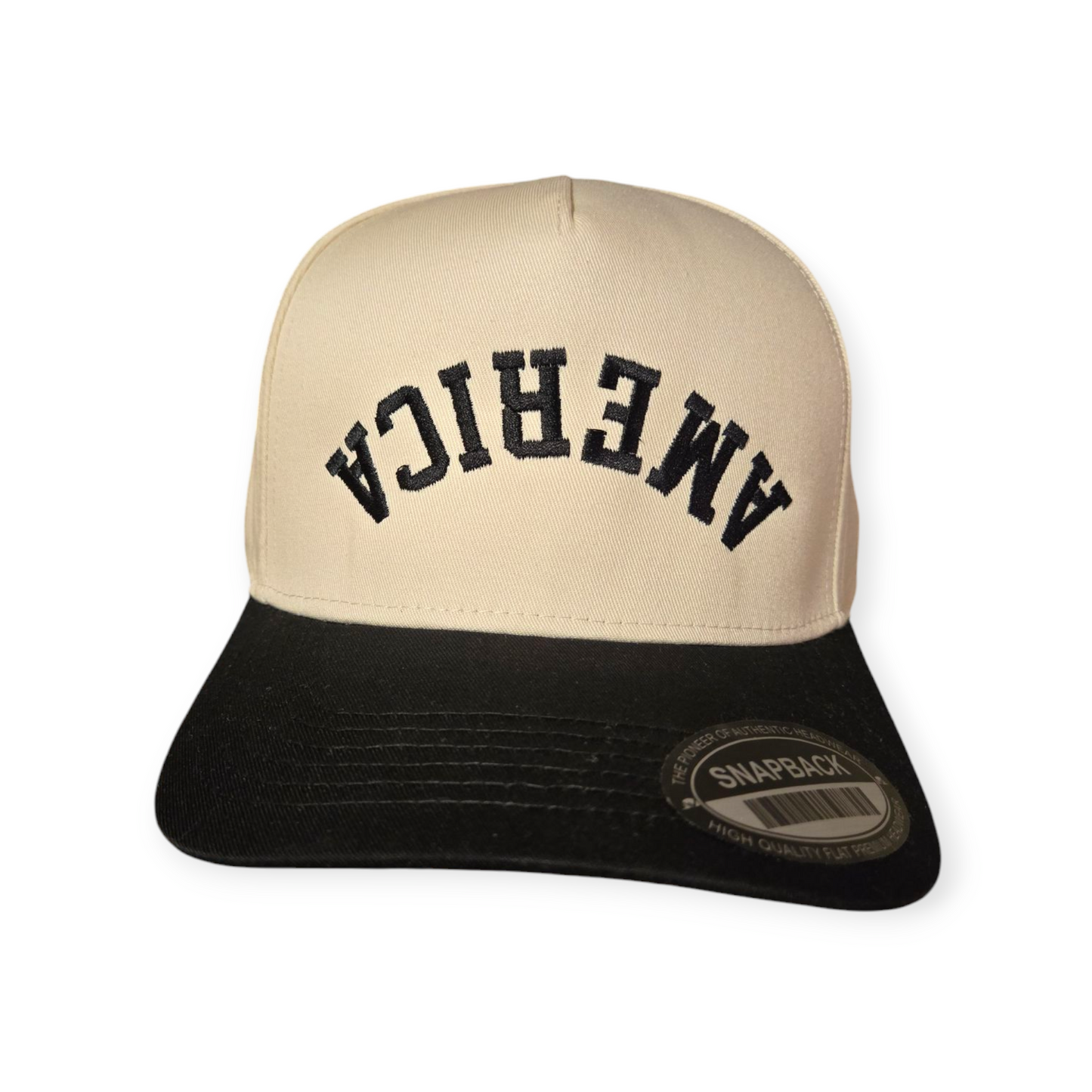 Front facing America Upside Down V1 structured hat in black and beige with the word “America” embroidered upside down in black on the front.