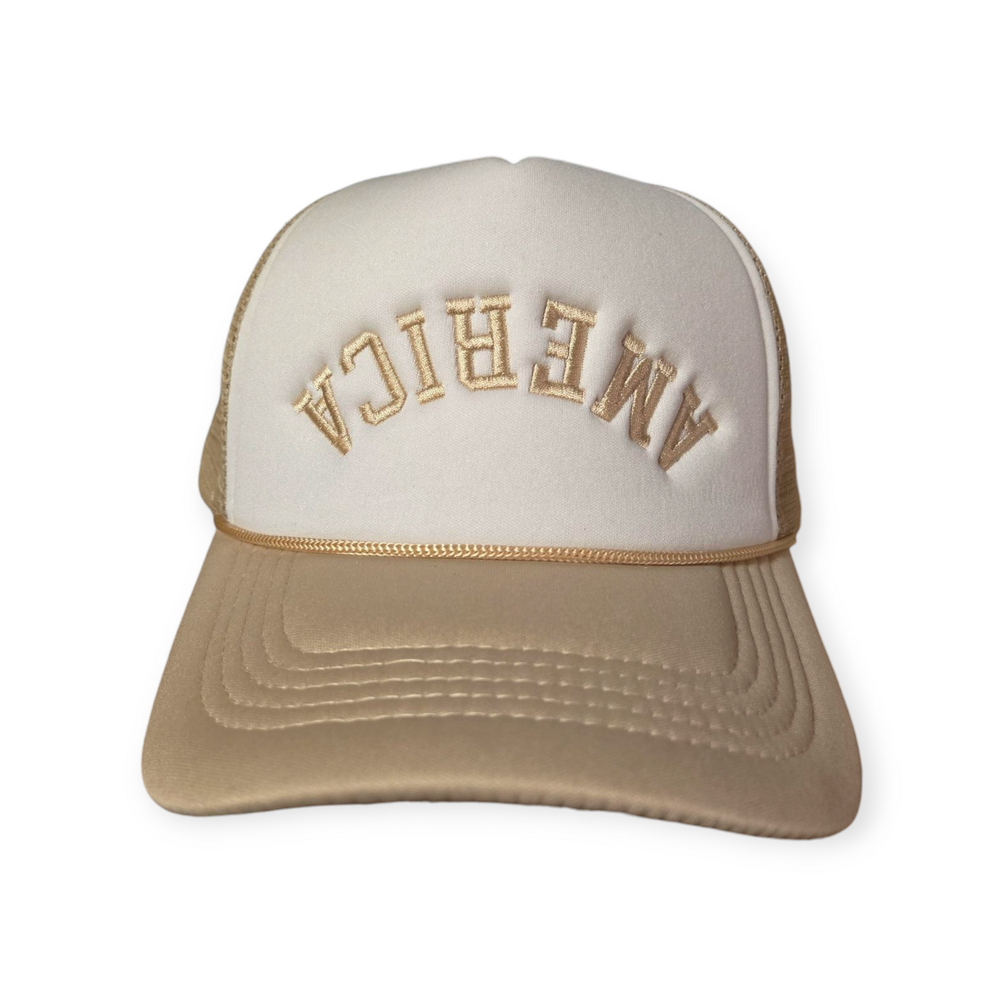Front facing America Upside Down V1 trucker hat in beige and white with the word “America” embroidered upside down in beige on the front.