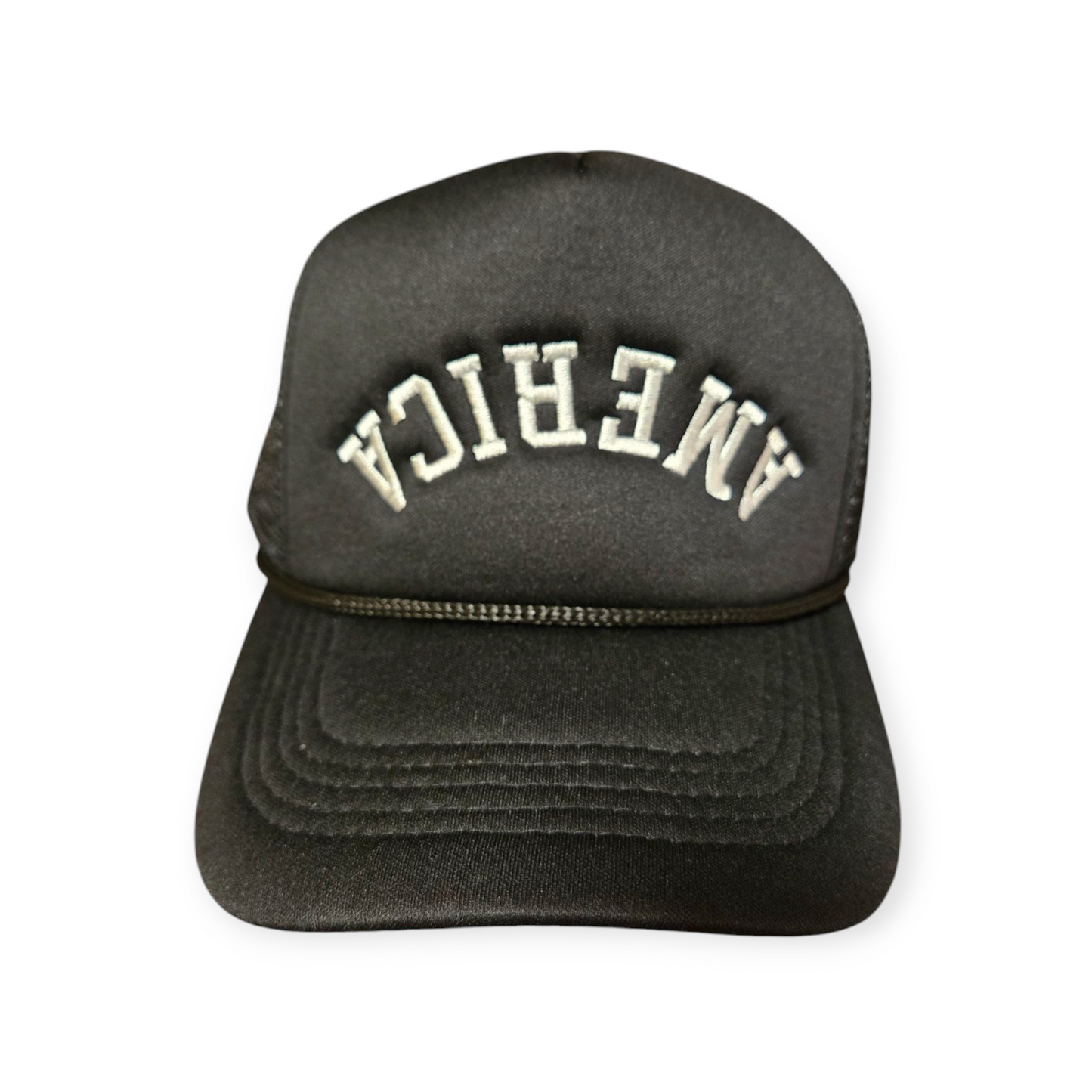 Front facing America Upside Down V1 trucker hat in black with the word “America” embroidered upside down in white on the front.