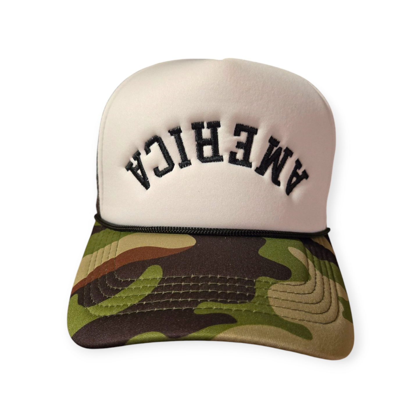 Front facing America Upside Down V1 trucker hat in camo and white with the word “America” embroidered upside down in black on the front.