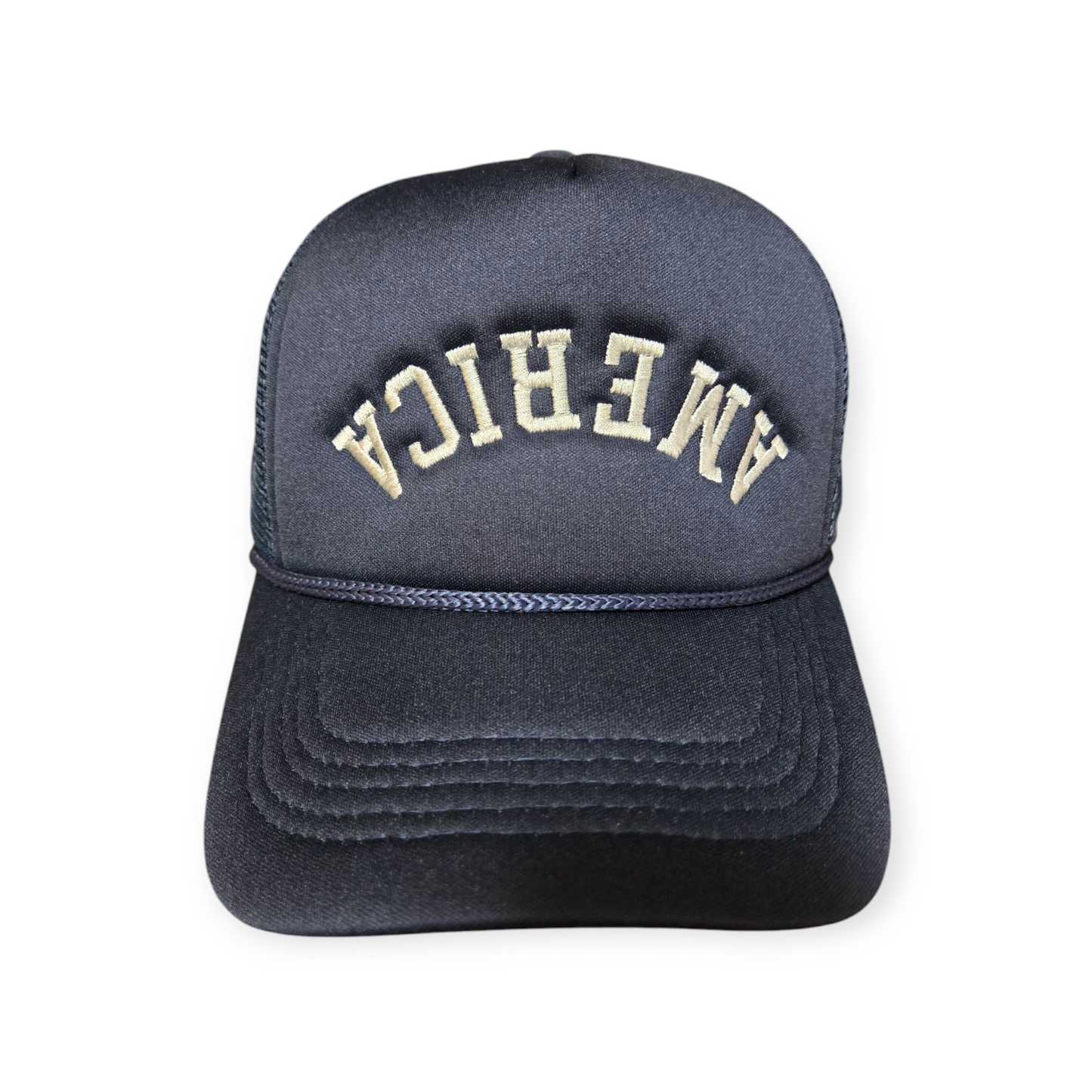 Front facing America Upside Down V1 trucker hat in navy blue and beige with the word “America” embroidered upside down in white on the front.