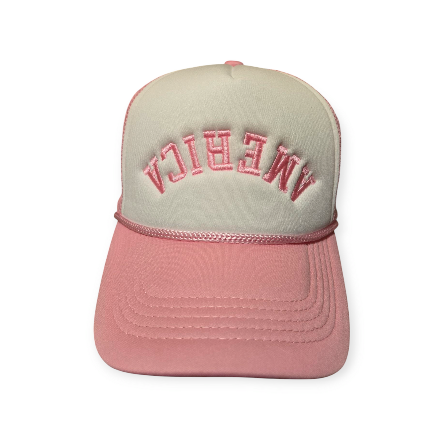 Front facing America Upside Down V1 trucker hat in pink and white with the word “America” embroidered upside down in pink on the front.
