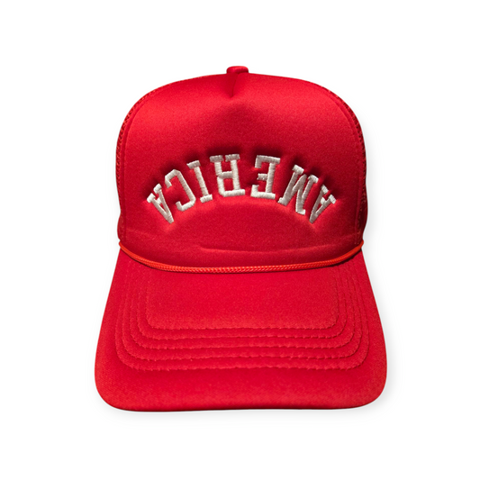 Front facing America Upside Down V1 trucker hat in red with the word “America” embroidered upside down in white on the front.