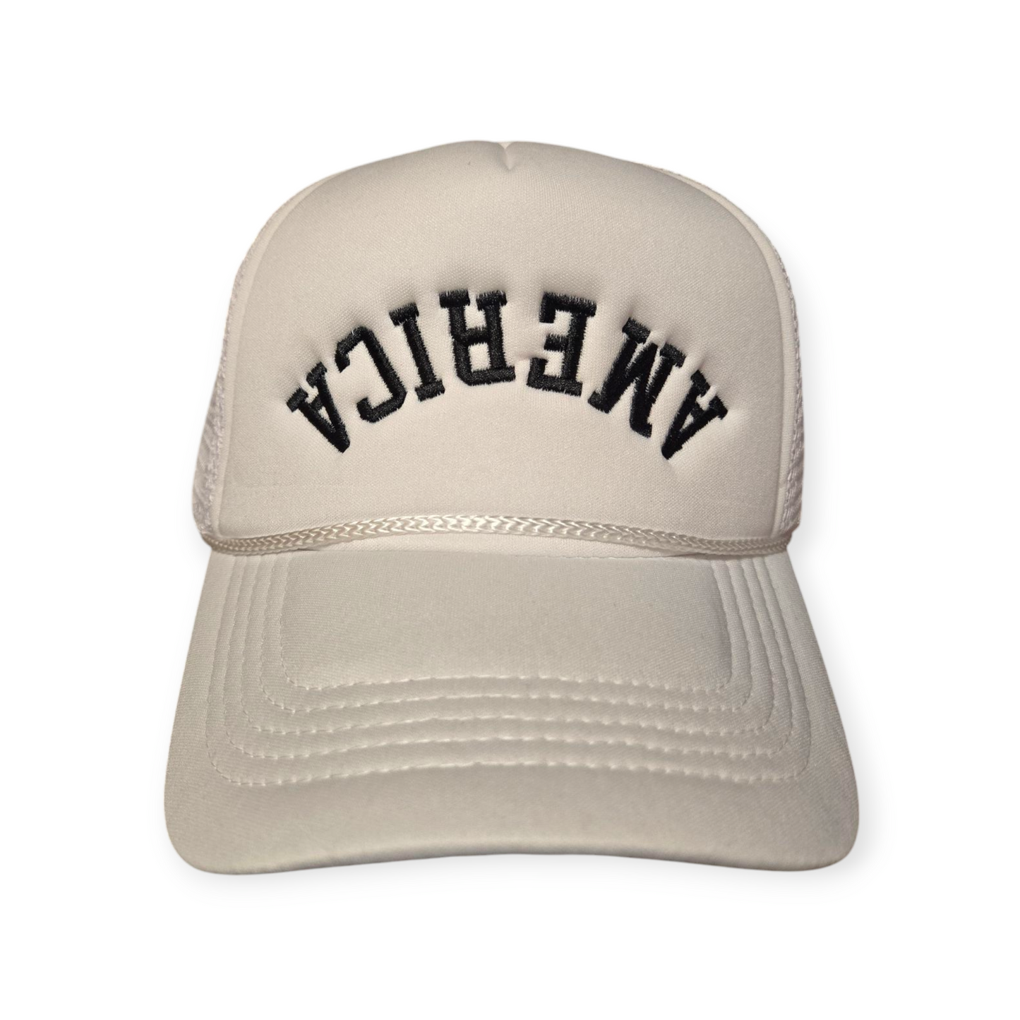 Front facing America Upside Down V1 trucker hat in white with the word “America” embroidered upside down in black on the front.
