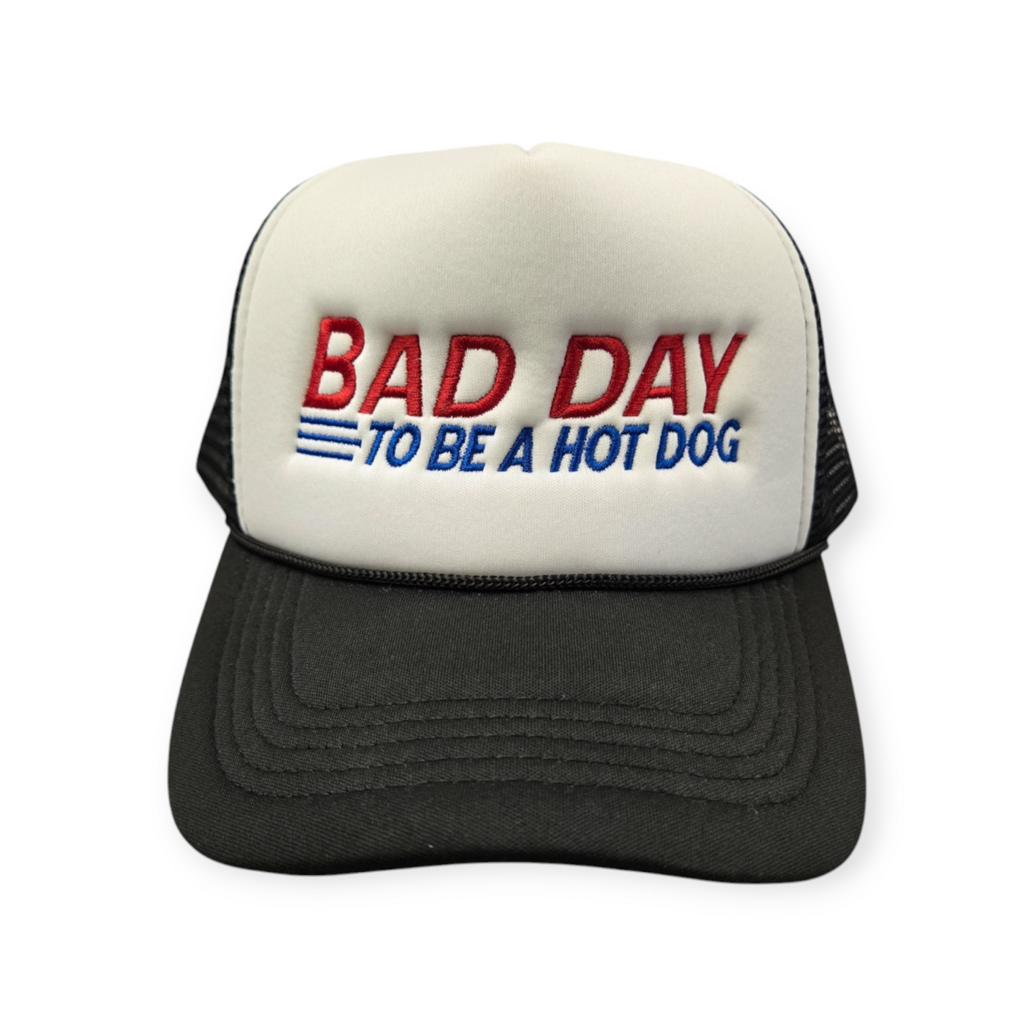 Front facing view of a black and white trucker hat with “Bad Day to Be a Hot Dog” embroidered in red and blue.