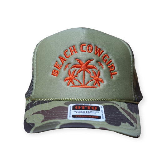 A camo-olive green trucker hat with burnt orange embroidery that says “Beach Cowgirl.”
