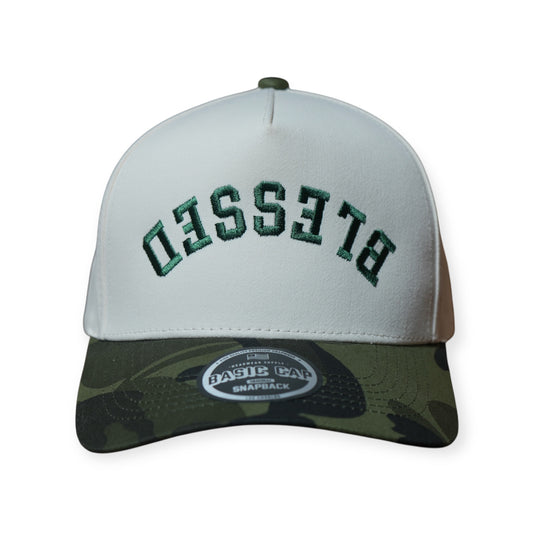 A camo and beige structured hat with forest green embroidery that says “Blessed” upside down.