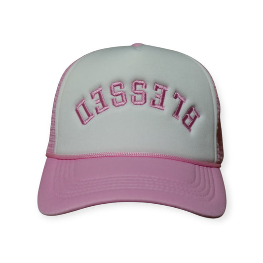 A pink and white trucker hat with pink embroidery that says “Blessed” upside down.