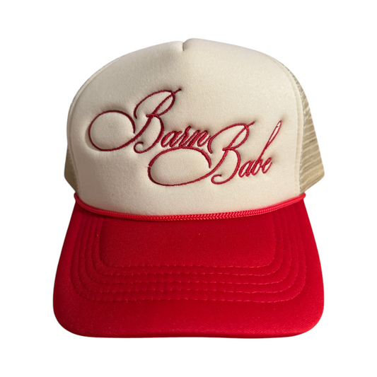 Front-facing red and beige trucker hat with a curved brim and mesh back, featuring “Barn Babe” embroidered in red across the front.