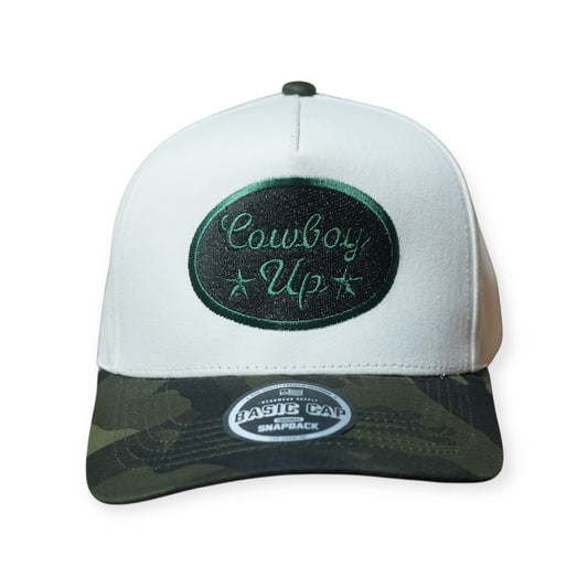 Camo and beige structured snapback hat with a curved brim and “COWBOY UP” embroidered across the front in black and forest green thread.