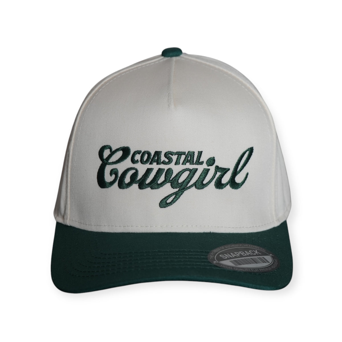 Front-facing Coastal Cowgirl V2 structured snapback hat with a beige crown, dark green bill and top button, featuring “Coastal Cowgirl” embroidered in dark green lettering across the front.
