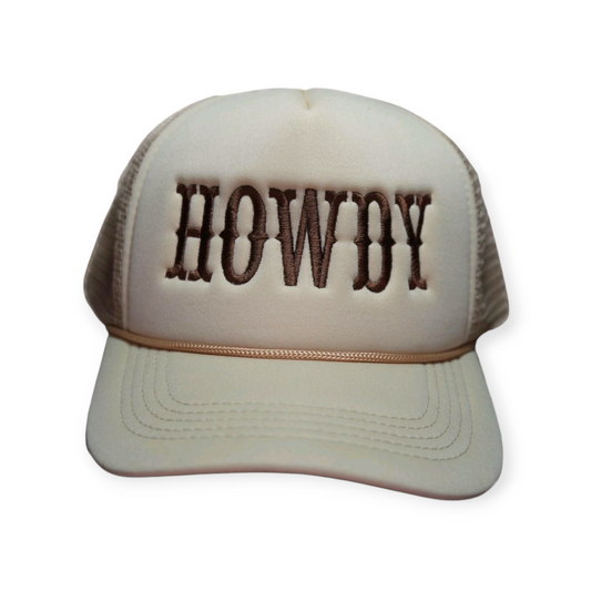 Beige trucker snapback hat with “HOWDY” embroidered across the front in dark brown thread.