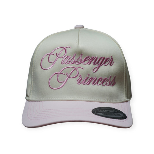 Pink and beige structured snapback hat with a curved brim and “PASSENGER PRINCESS” embroidered across the front in pink thread.